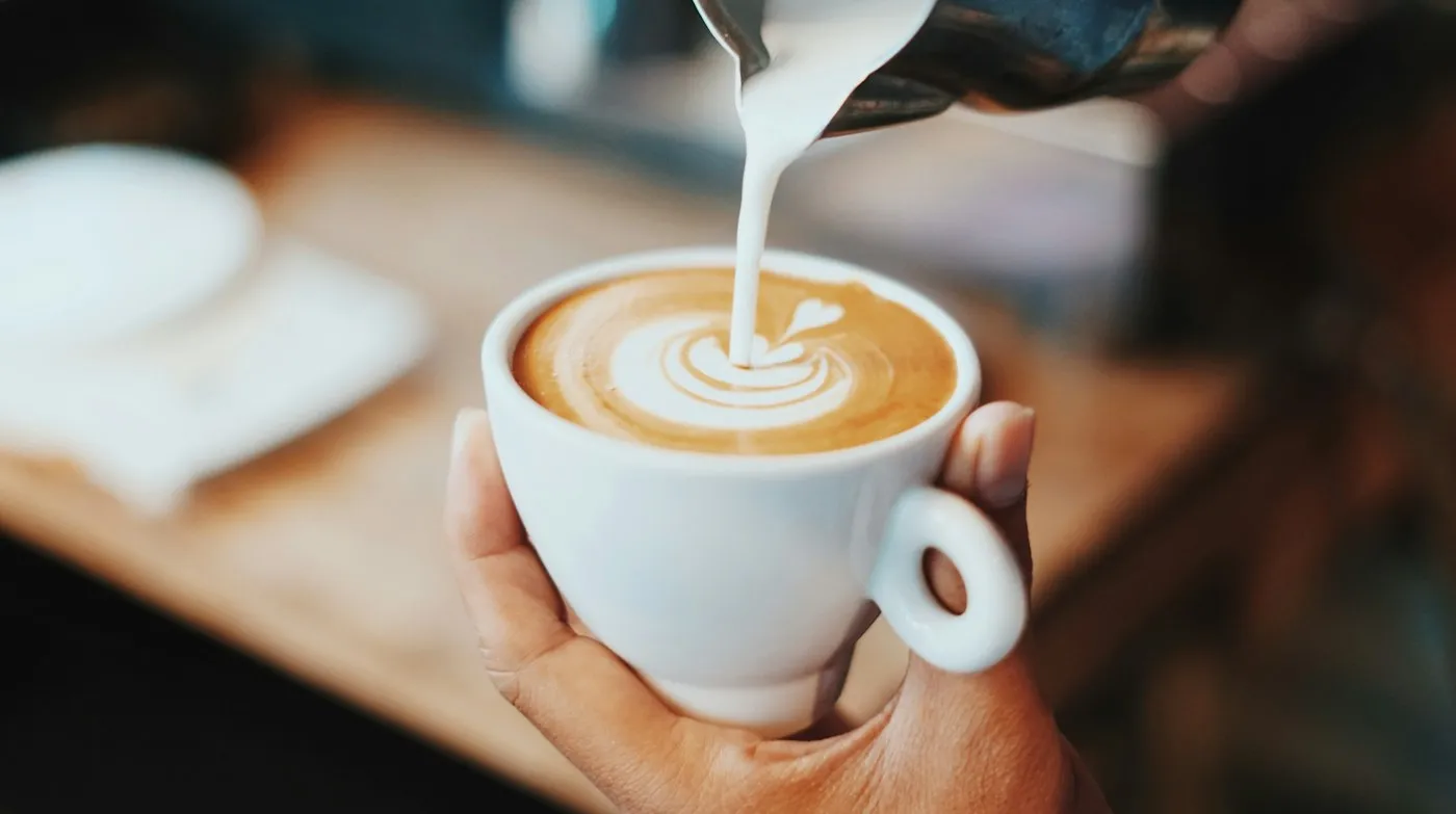 Barista pouring latte art into a hot latte
