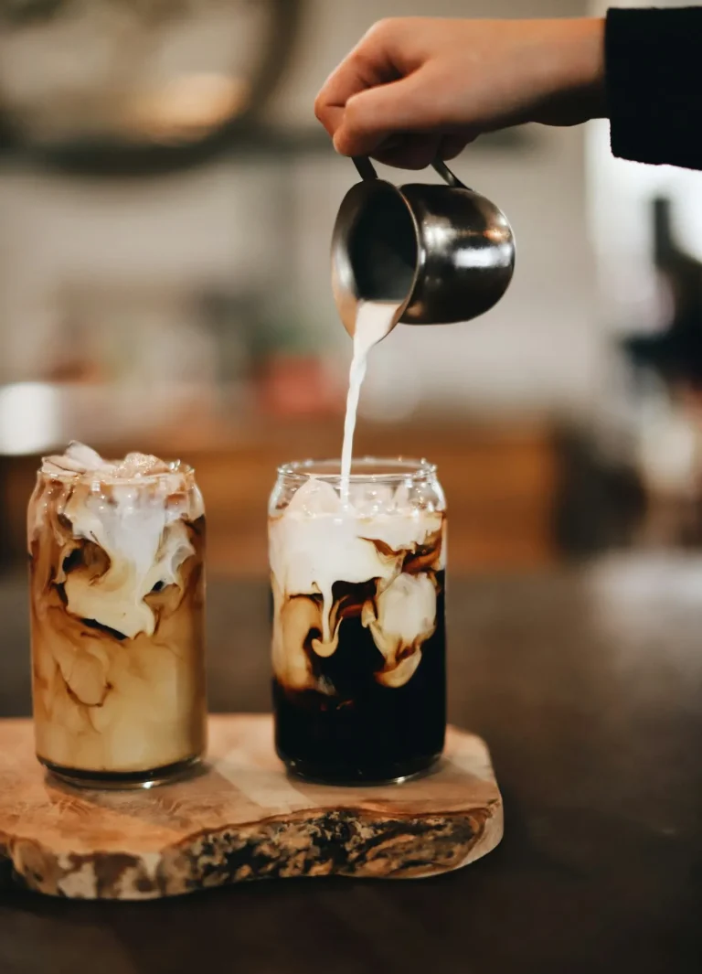Cream being poured into a glass of iced coffee to make a breve-style drink